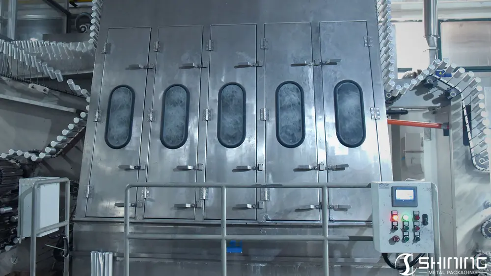 Botellas de aluminio pasando por una lavadora especializada para desengrasarlas y limpiarlas.