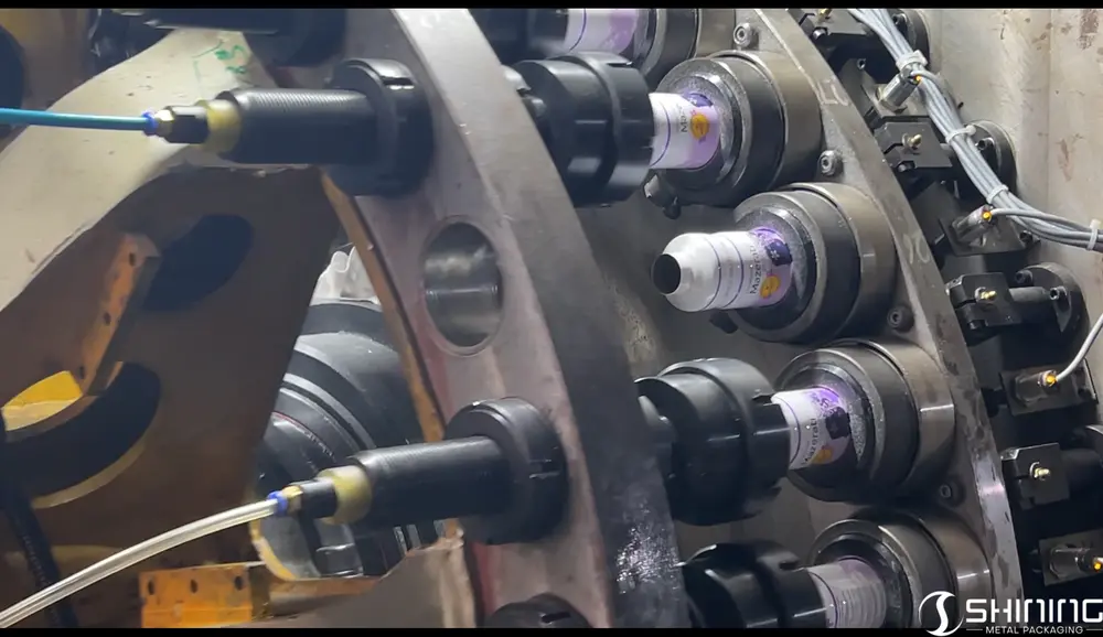 Una máquina que va dando forma gradualmente al hombro y al cuello de una botella de aluminio preimpresa.