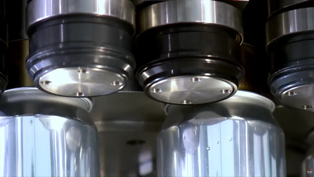 Comprendre le processus de double sertissage dans la fabrication des boîtes de conserve 8 Gros plan sur les mandrins et les rouleaux de sertissage scellant des canettes de boisson en aluminium sur une ligne de sertissage double rotative. Titre : Gros plan sur la tête de sertissage : mandrin et rouleaux scellant des canettes en aluminium