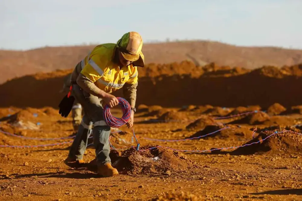 Worker installing red and blue twisted pair blasting wire in mining site with PVC insulated copper conductor