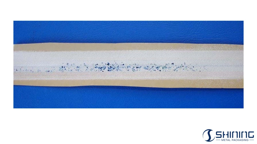Close-up of a tinplate substrate showing blue spots that indicate individual coating pores revealed by an electrical conductivity test.